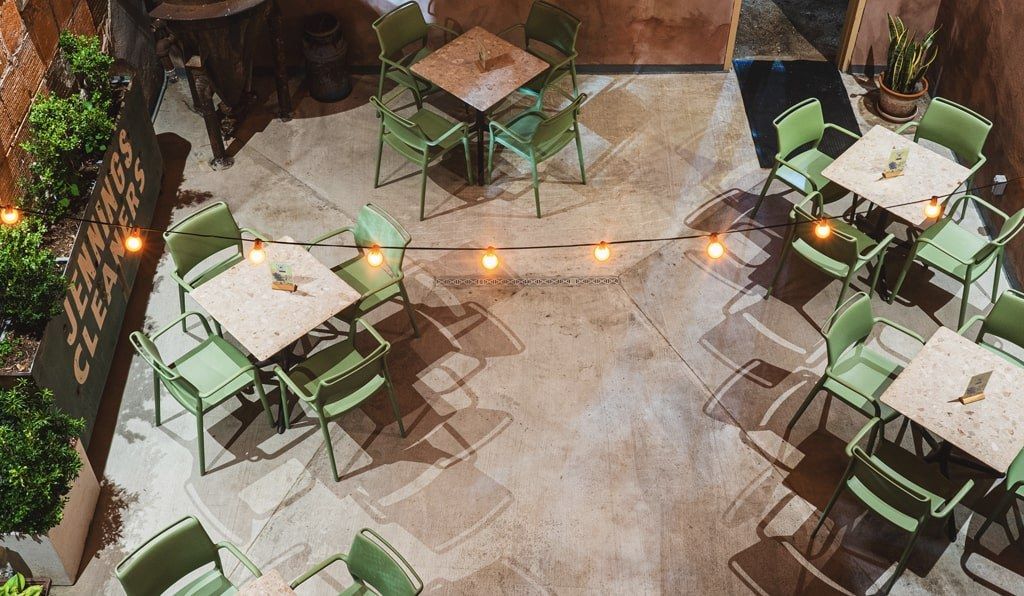 Outdoor patio seen from above with green chairs, small tables and string lights