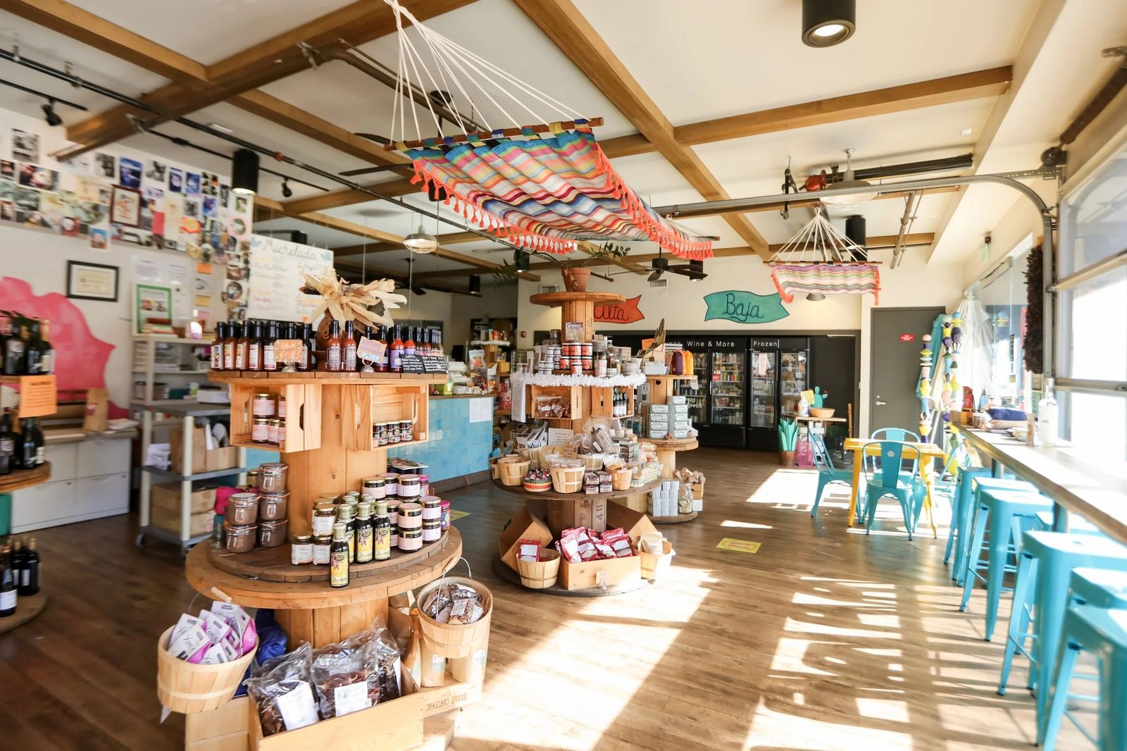 A market hall with wood-beamed ceiling, shelves of goods and a turquoise counter, lit by windows.