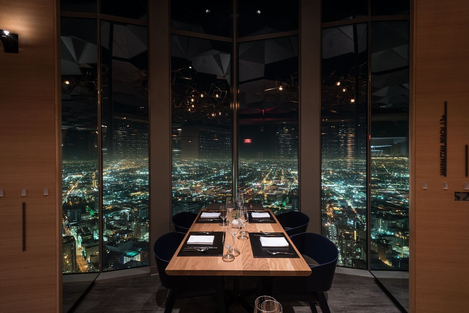 A table set for dinner beside floor-to-ceiling windows overlooking city lights at night.