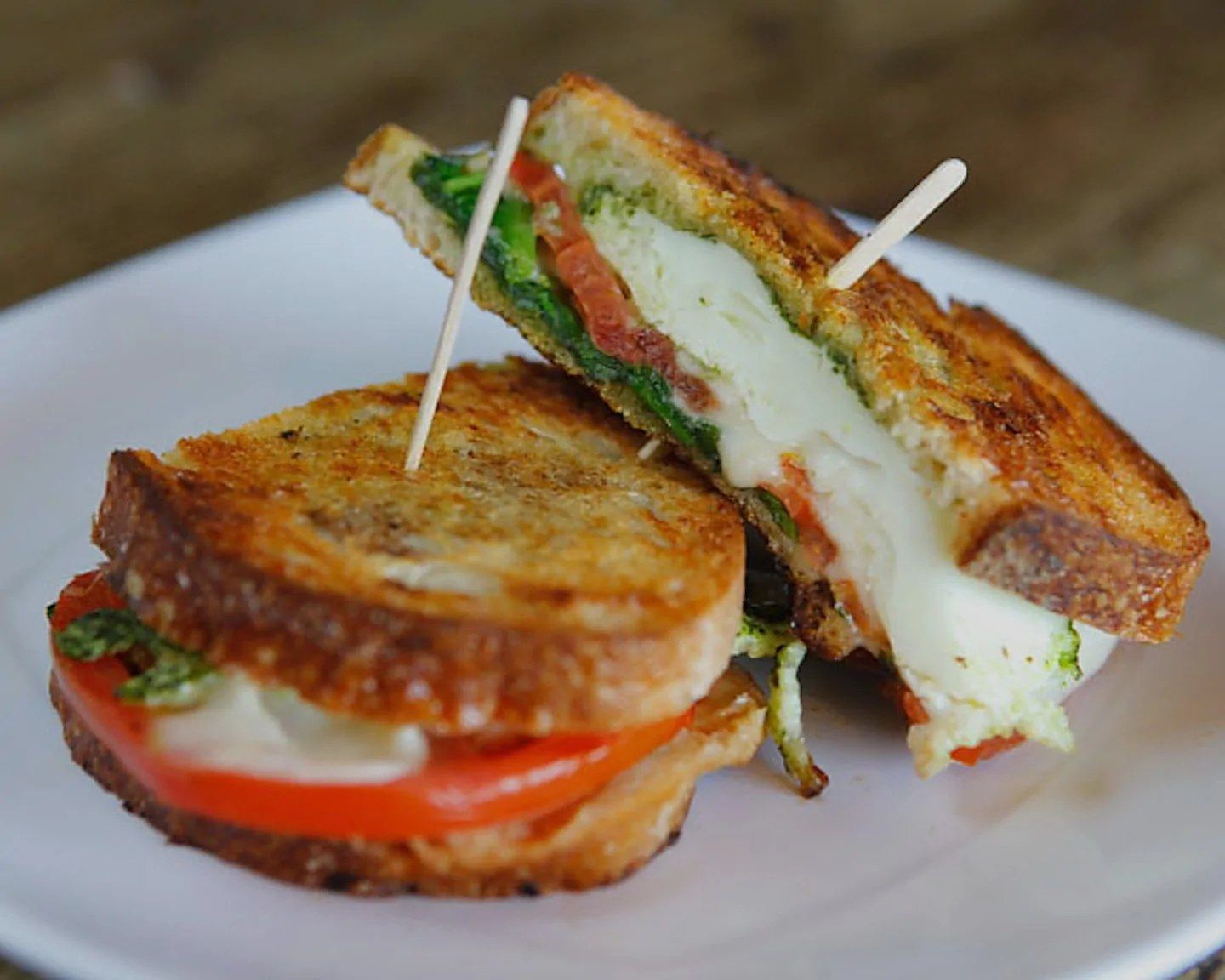 A grilled sandwich with melted cheese and tomato, cut in half on a plate.