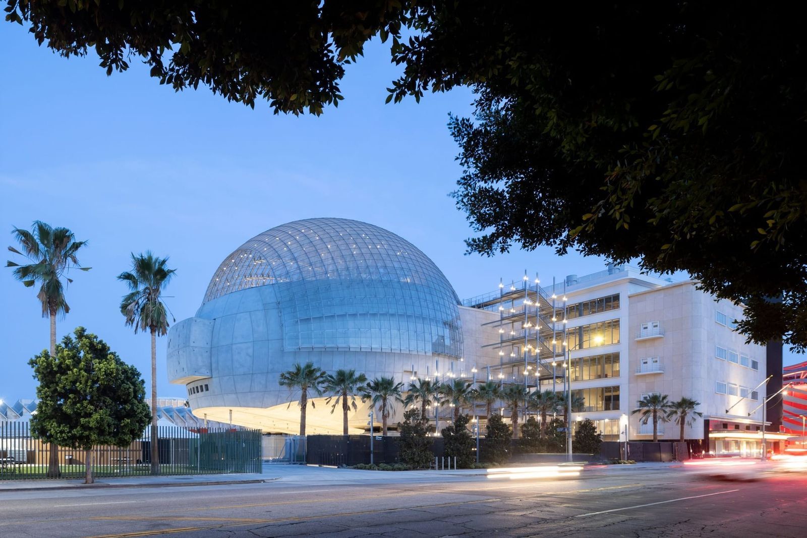 A large glass sphere atop a building with palm trees in front, at dusk.