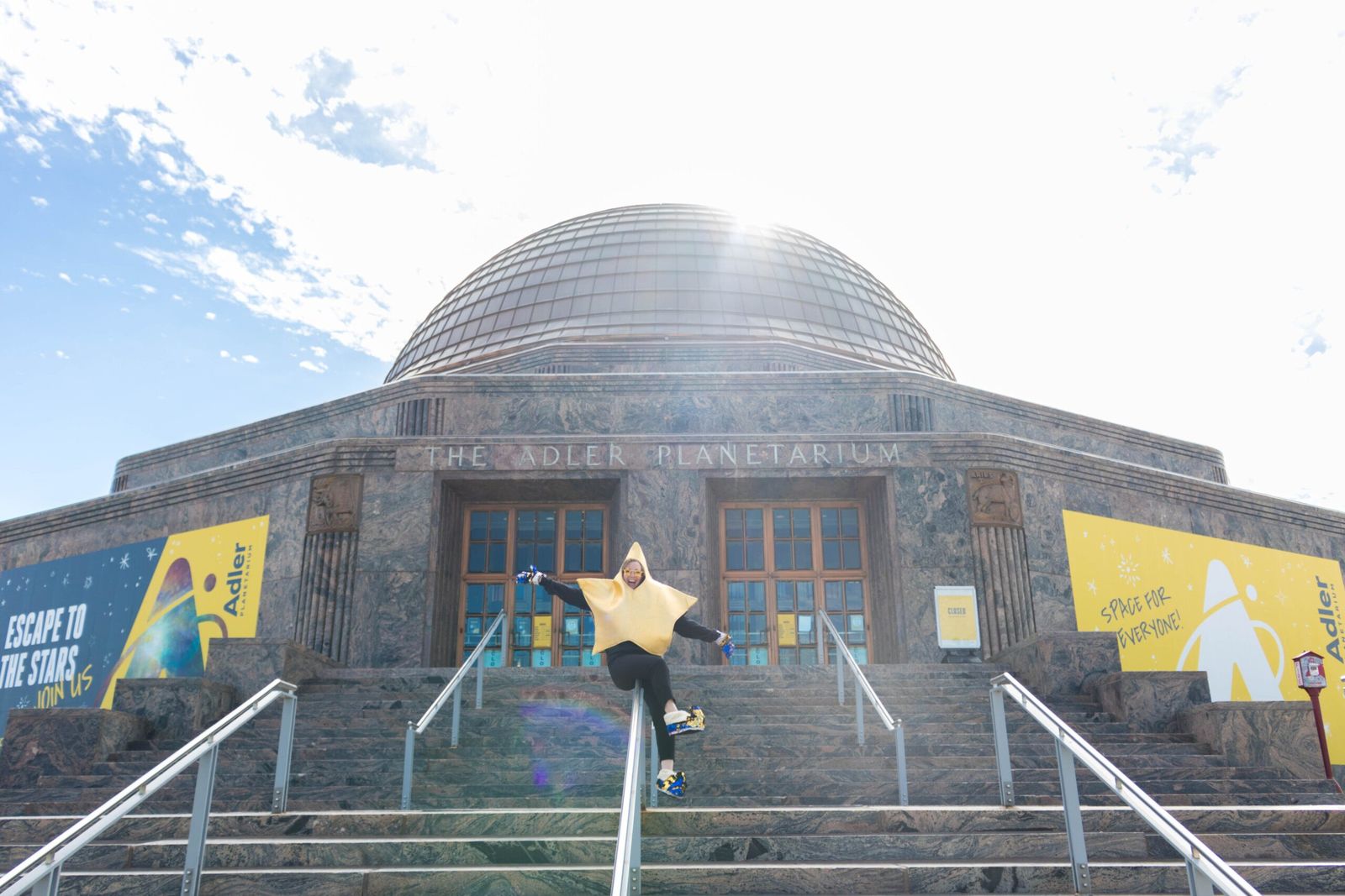 The planetarium's domed stone building at the top of a staircase with a person leaping on the steps, under a bright sky.