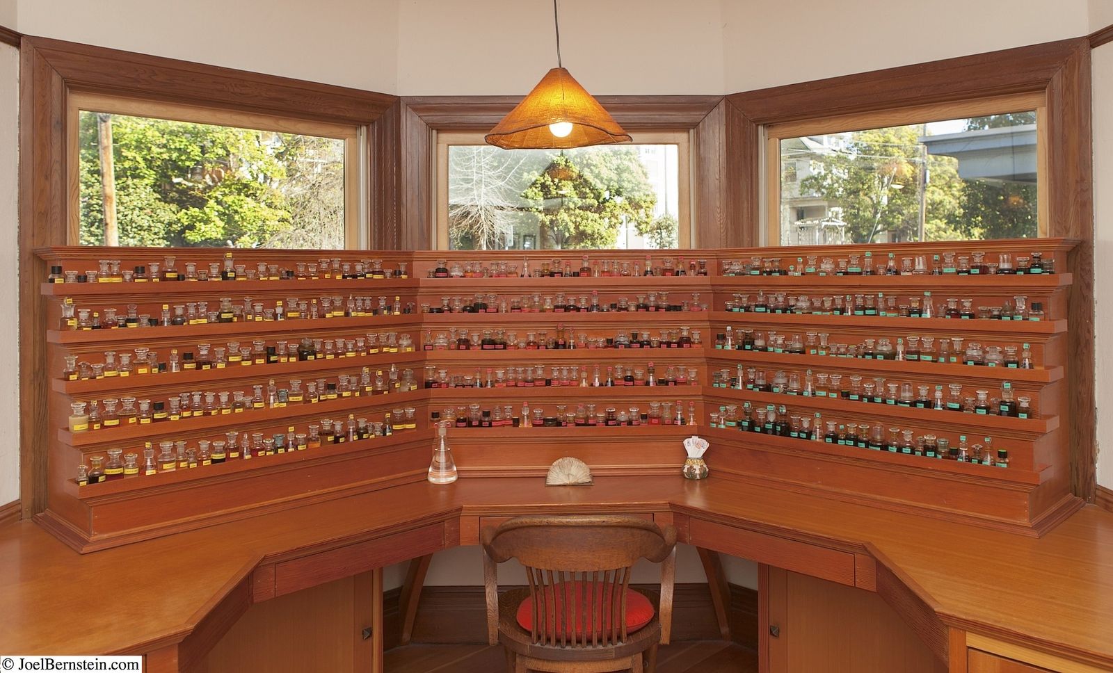 A wooden perfumer's cabinet with rows of small drawers and bottles under a bay of windows.
