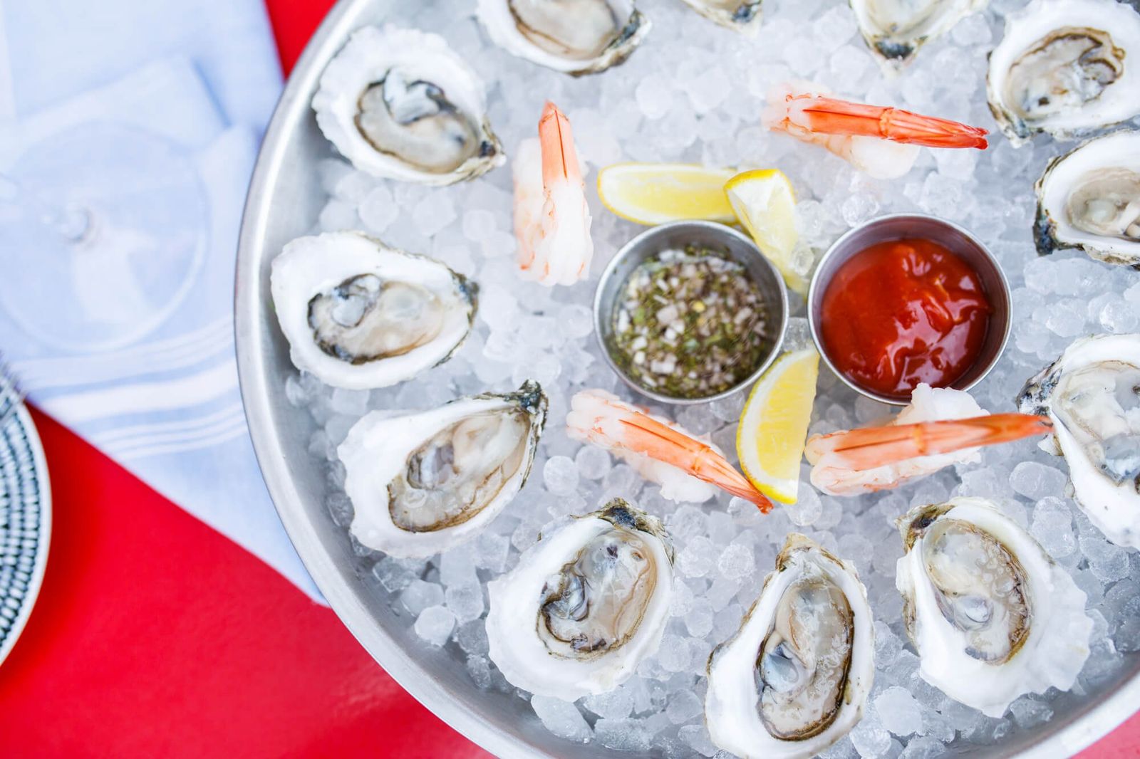 Silver platter of oysters on ice with lemon, shrimp and small cups of sauce