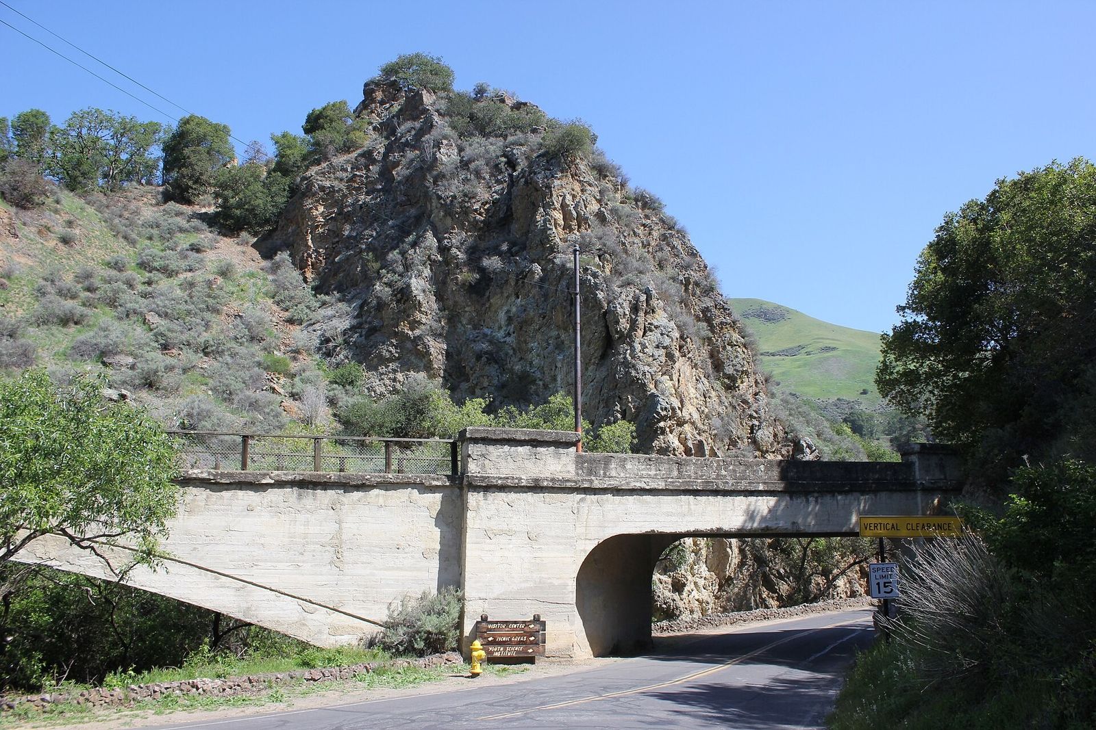 Narrow road passing under a concrete bridge beside a rocky hillside in a park