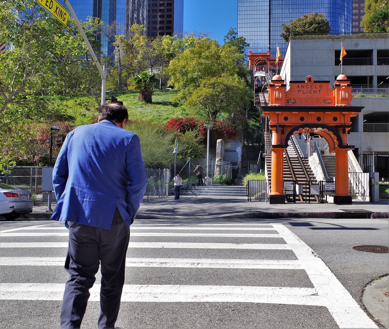 A man in a blue jacket crossing a street toward the orange arched entrance of Angels Flight railway