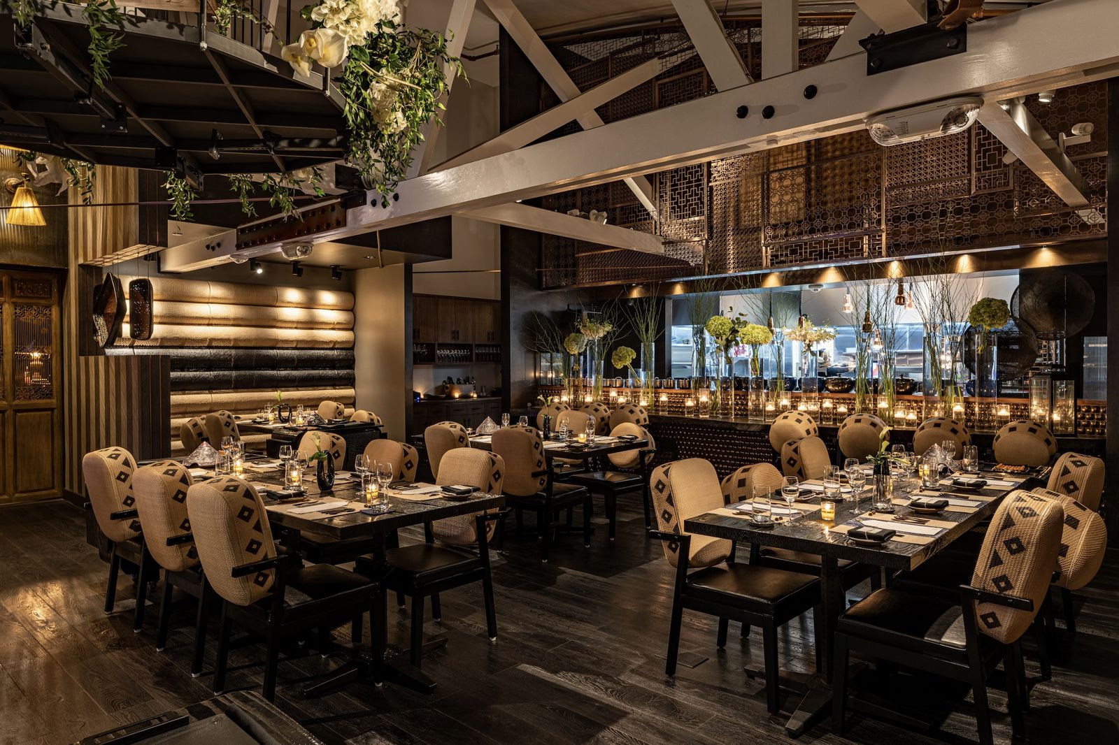 A large dining room with rows of set tables and chairs under a high ceiling with hanging greenery.