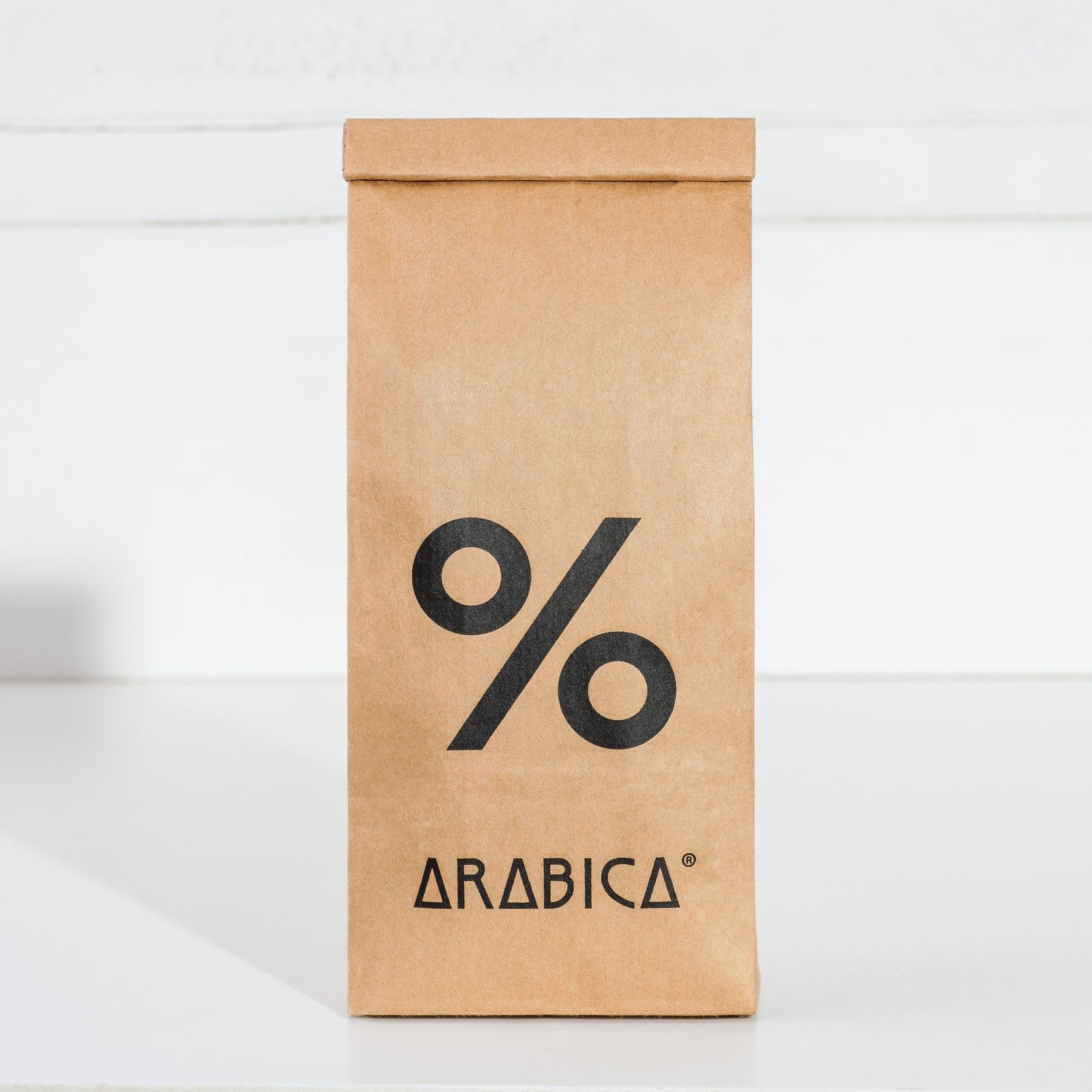 A kraft paper bag of % Arabica coffee standing upright against a white background.