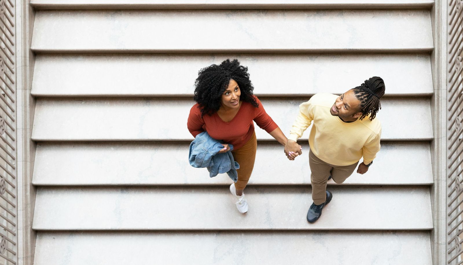 Two visitors holding hands seen from above on a wide white staircase.