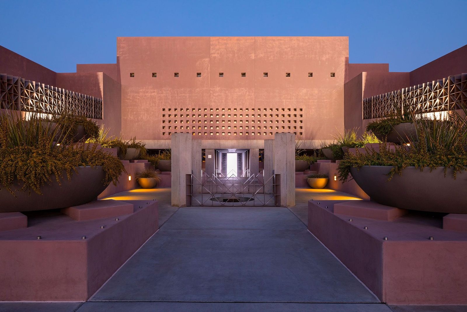 Pink stone museum entrance with planters and a lit doorway at dusk