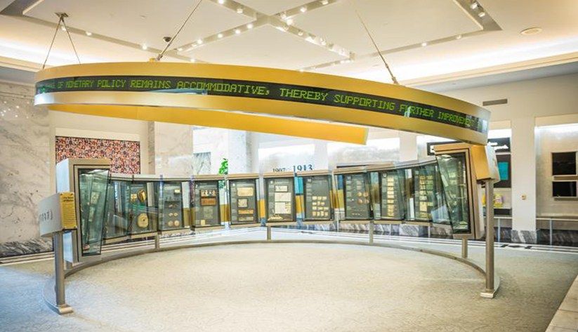A curved glass exhibit case ringing a museum gallery with a yellow banner overhead