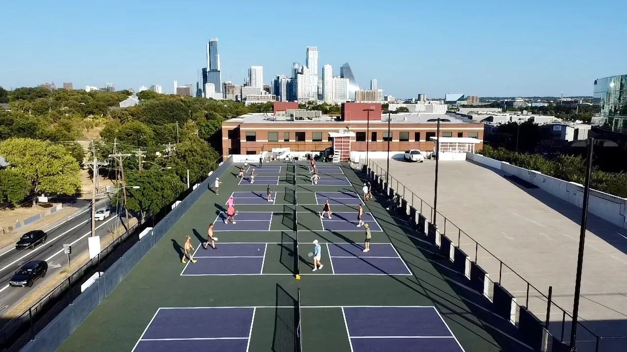 An aerial view of a row of pickleball courts on a rooftop with the Austin skyline behind.