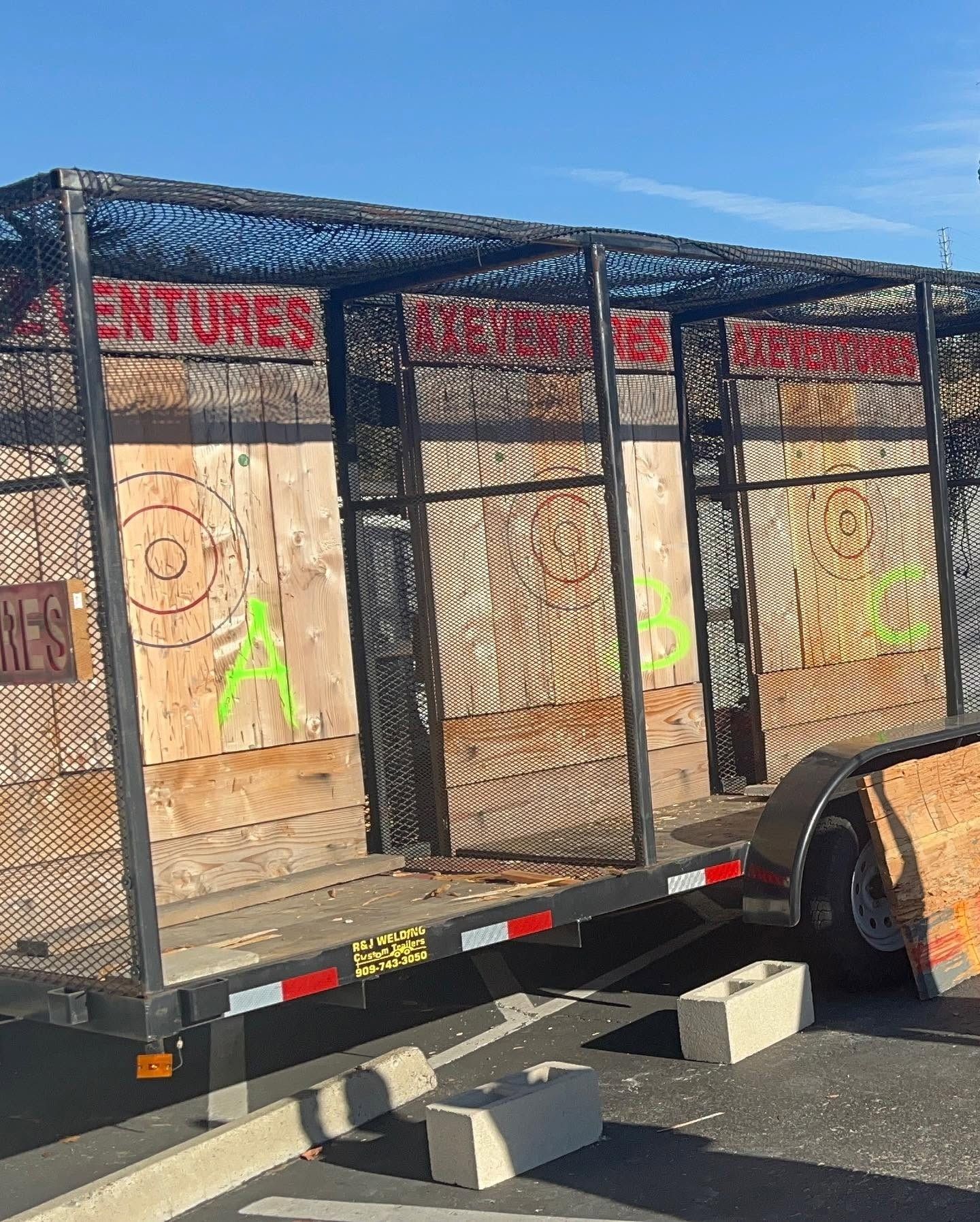 A trailer with plywood axe-throwing lanes painted with targets under a blue sky.