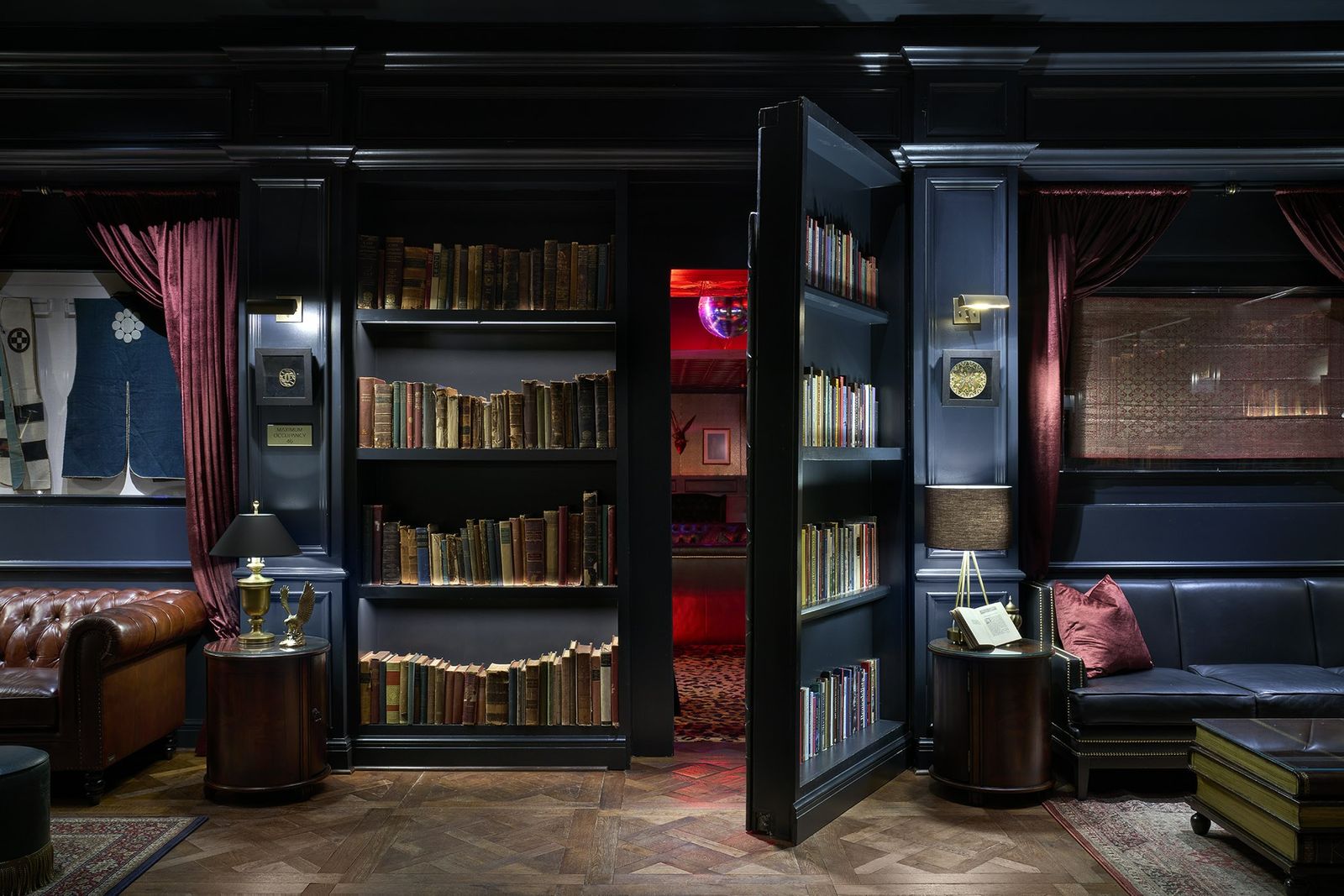 A dim lounge with leather sofas and built-in bookcases, one bookcase swung open like a door.