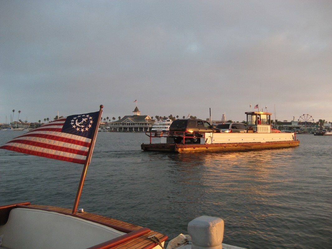 A small car ferry crossing the bay at dusk with an American flag in the foreground.