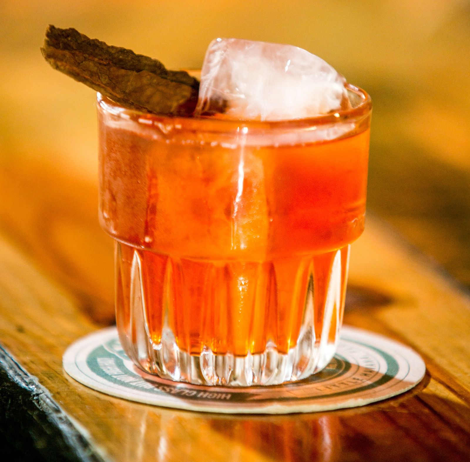 Orange cocktail over ice with a dried garnish on a coaster