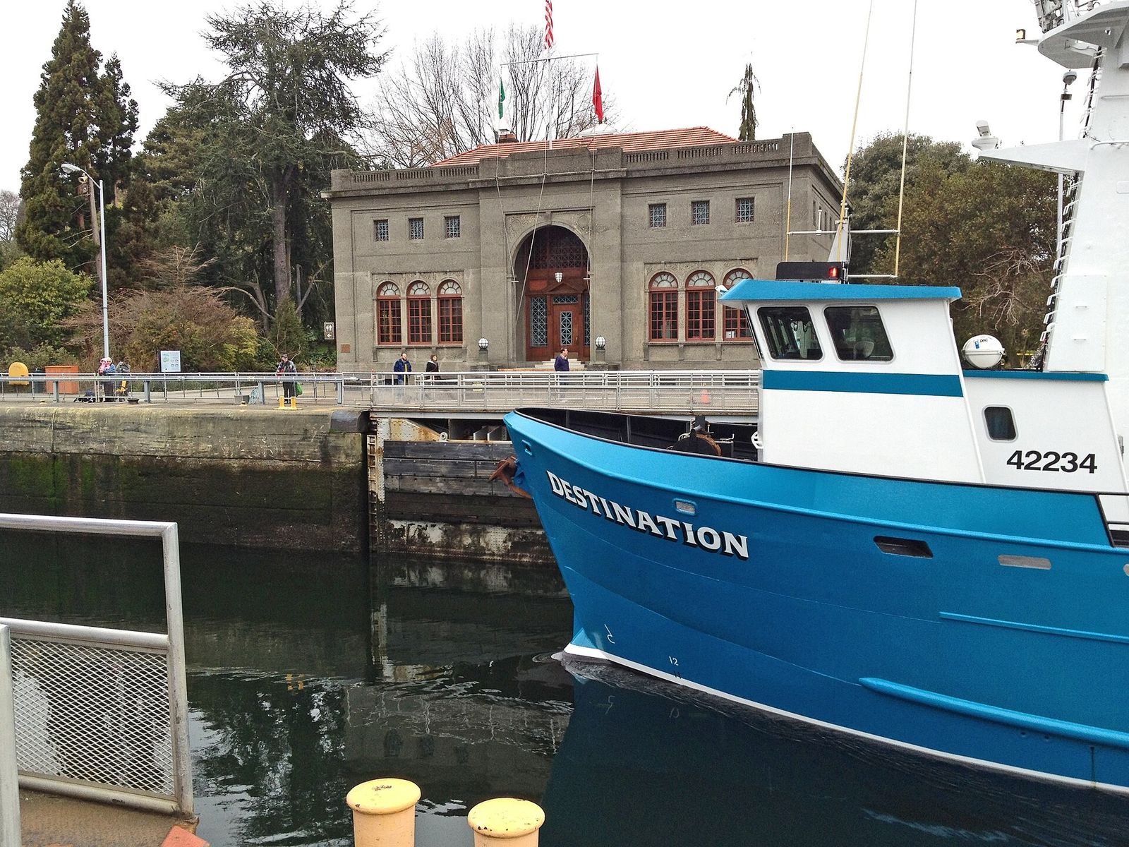 A stone administration building with arched windows beyond a blue fishing boat moored in the locks.