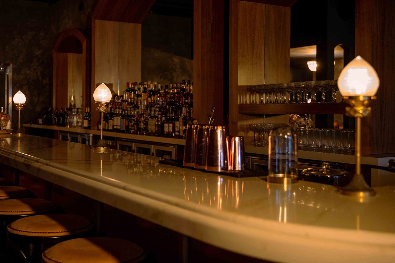A long bar counter lit by glowing lamps with bottles on the back shelves.