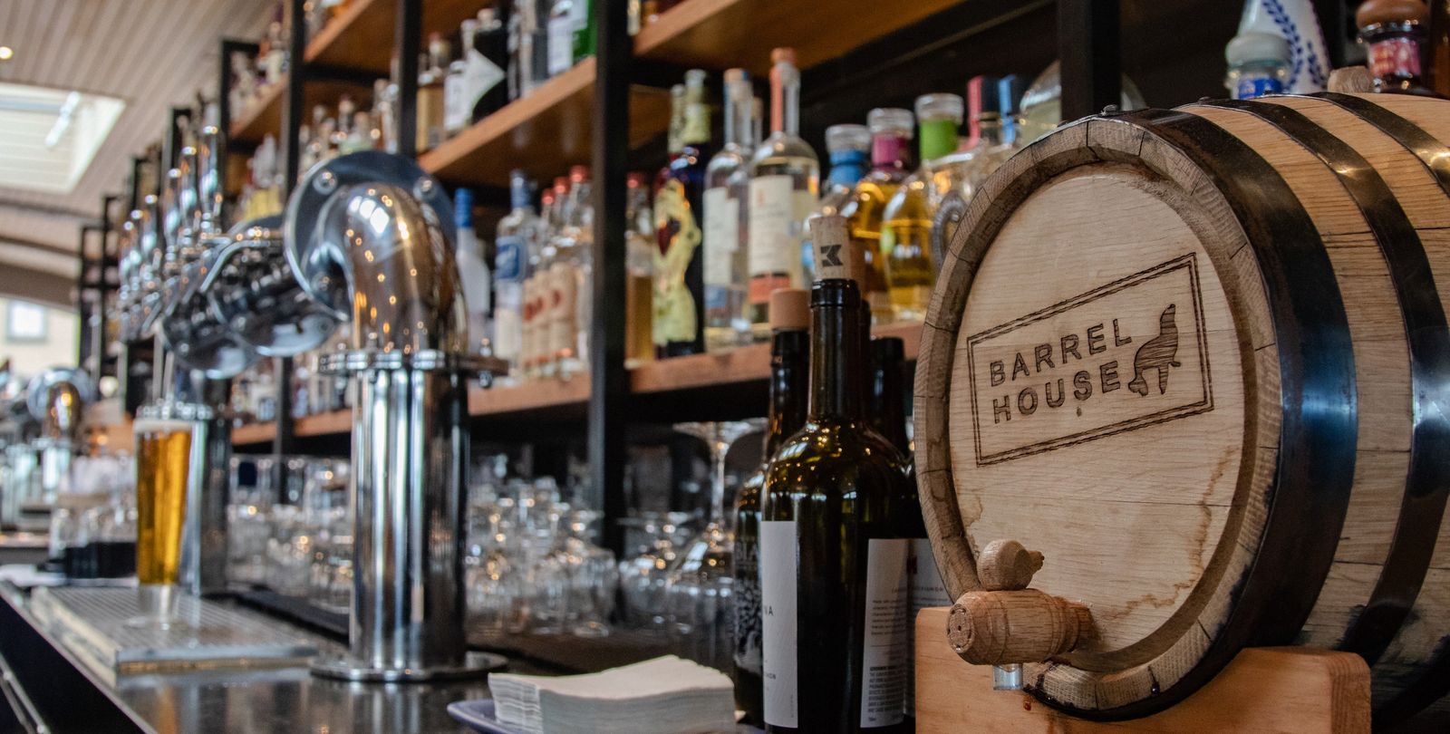 Bar back with taps, bottles on shelves and a Barrel House branded barrel