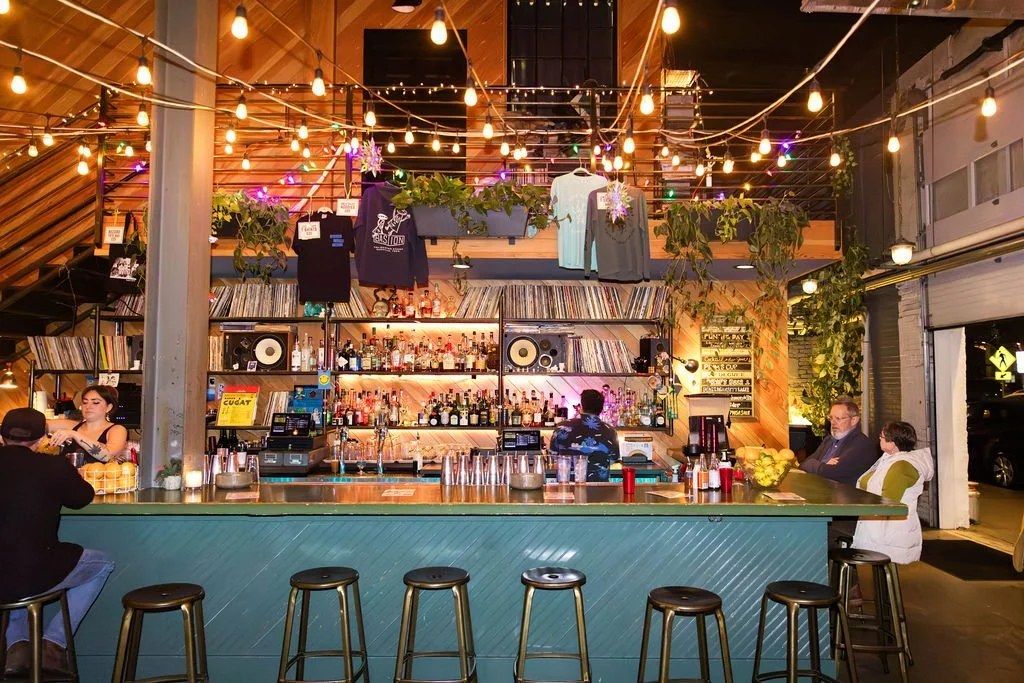 Bar with teal front and stools under string lights, shelves of records and bottles behind