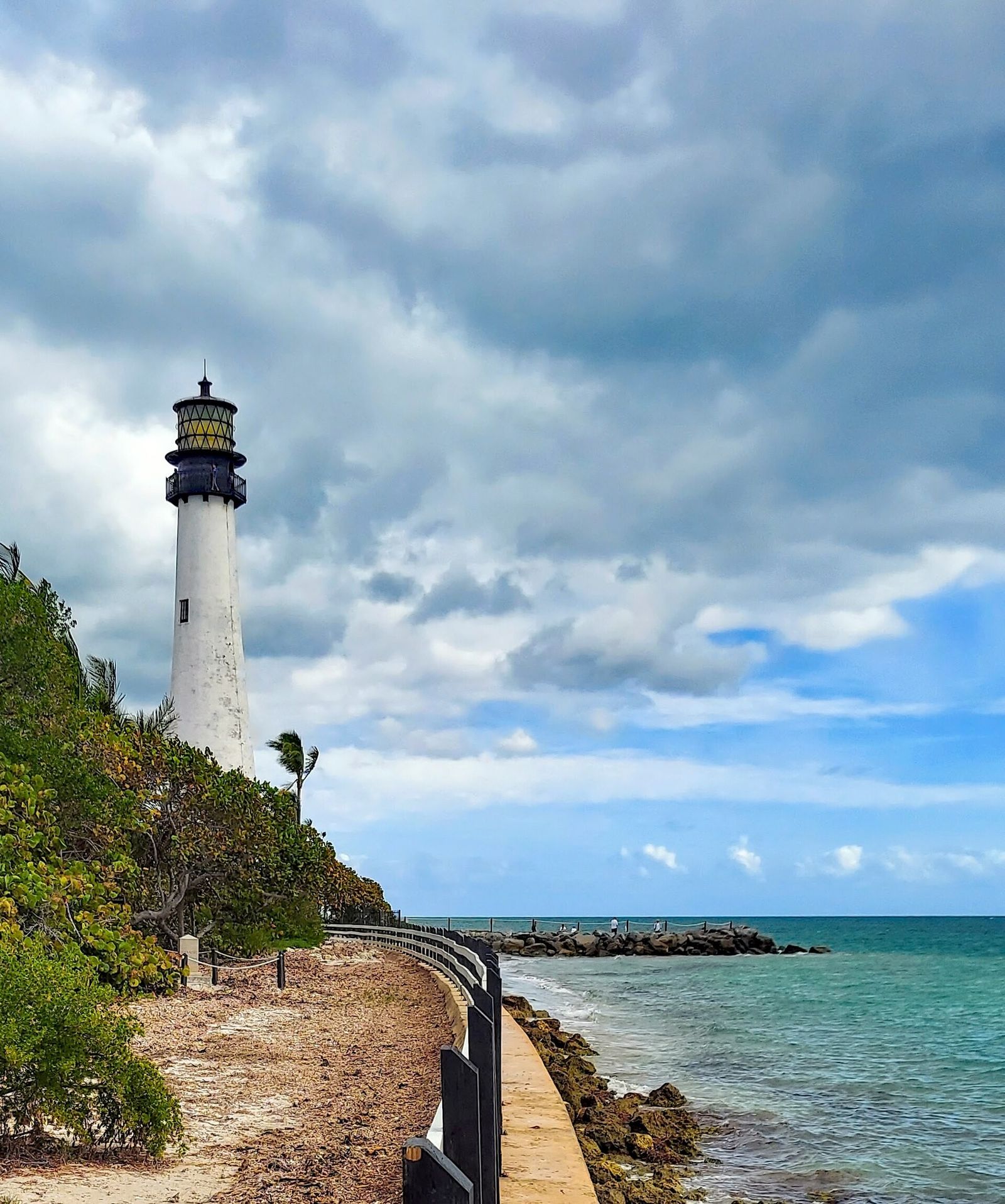 The Cape Florida lighthouse on a coastal bluff above turquoise water under a cloudy sky