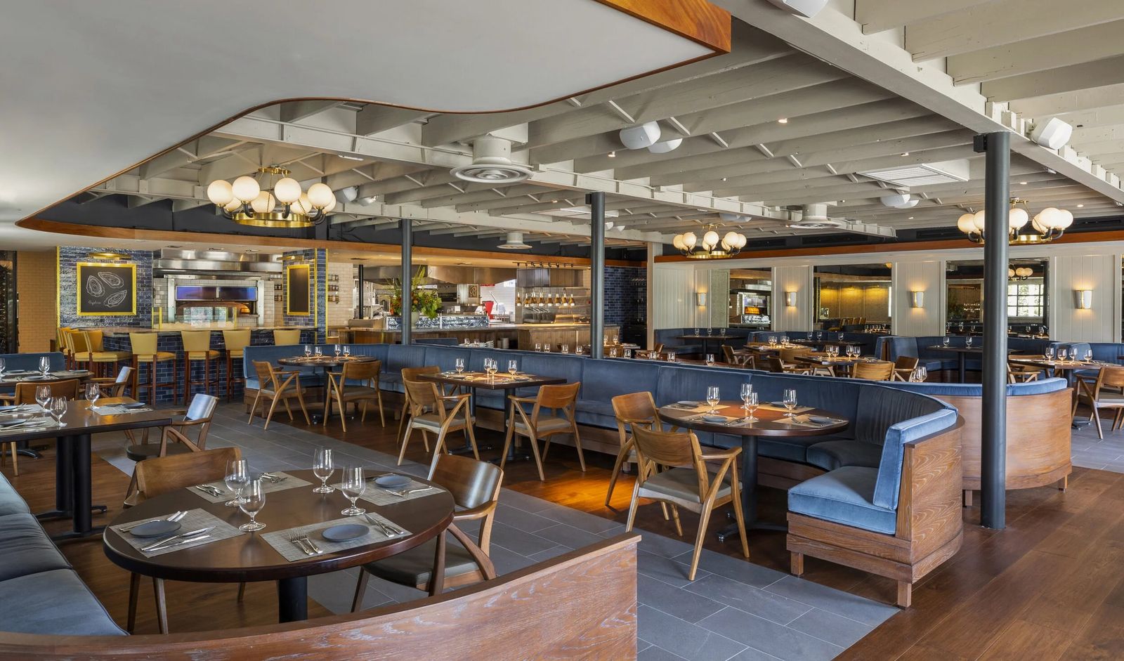 Bright dining room with tables, chairs and blue banquettes under a curved ceiling