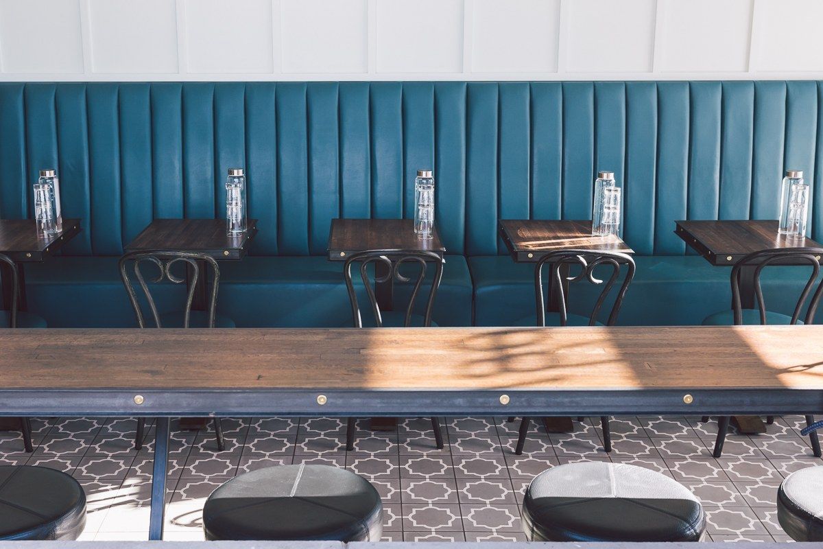 A row of teal tufted booth seating with wooden tables and bottles of water in a bright cafe.