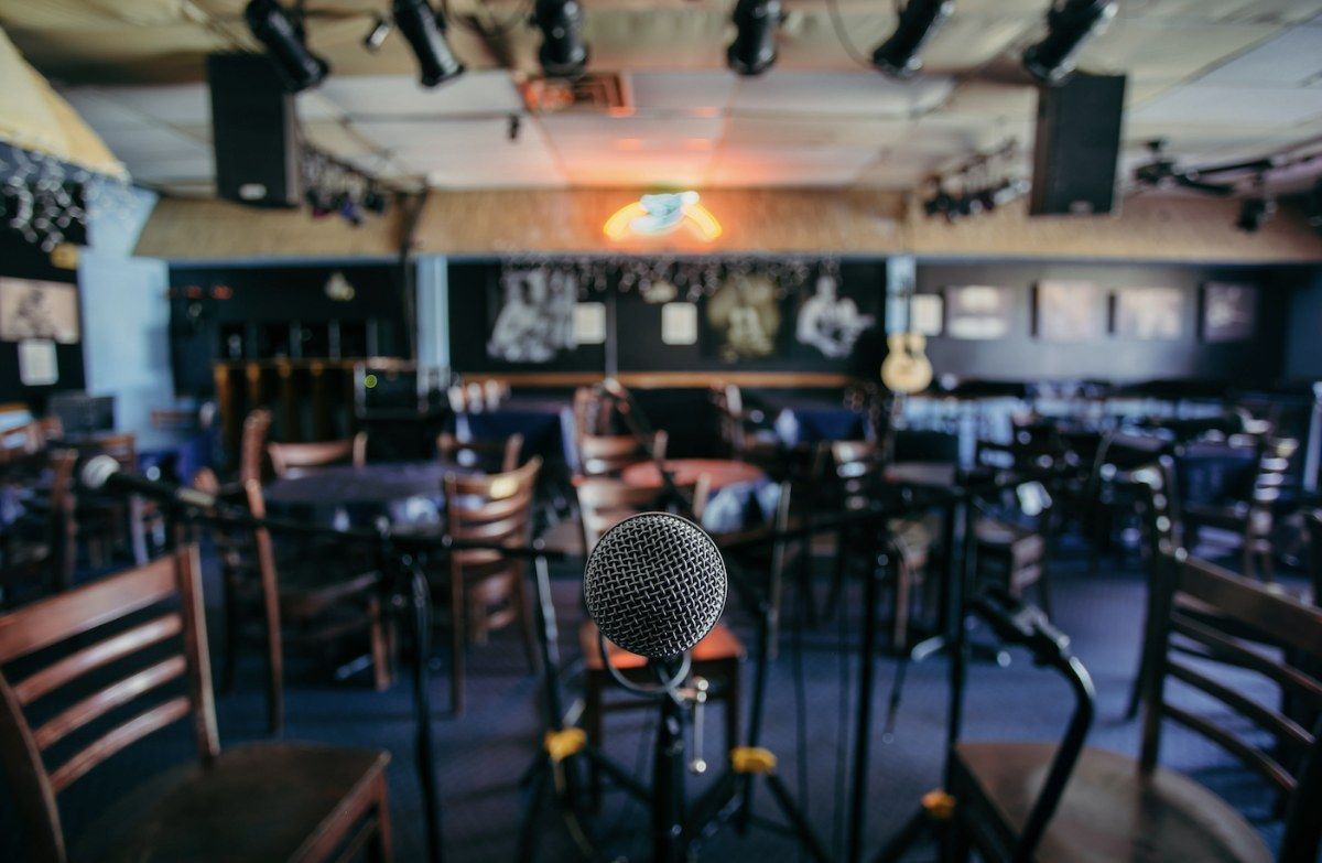 Small music room with rows of tables and chairs facing a stage with a microphone stand