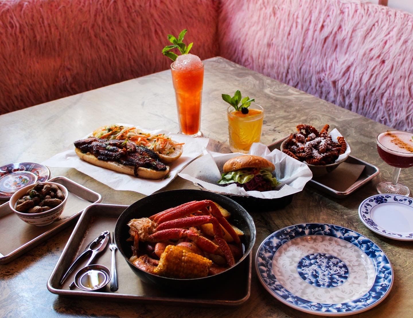 A table of Southeast Asian dishes and iced drinks on a pink fuzzy booth