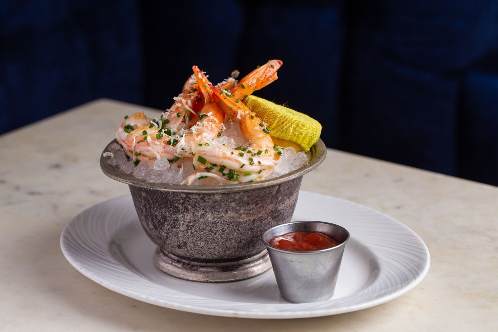 Seafood tower on ice in a metal bowl with cocktail sauce on a marble table