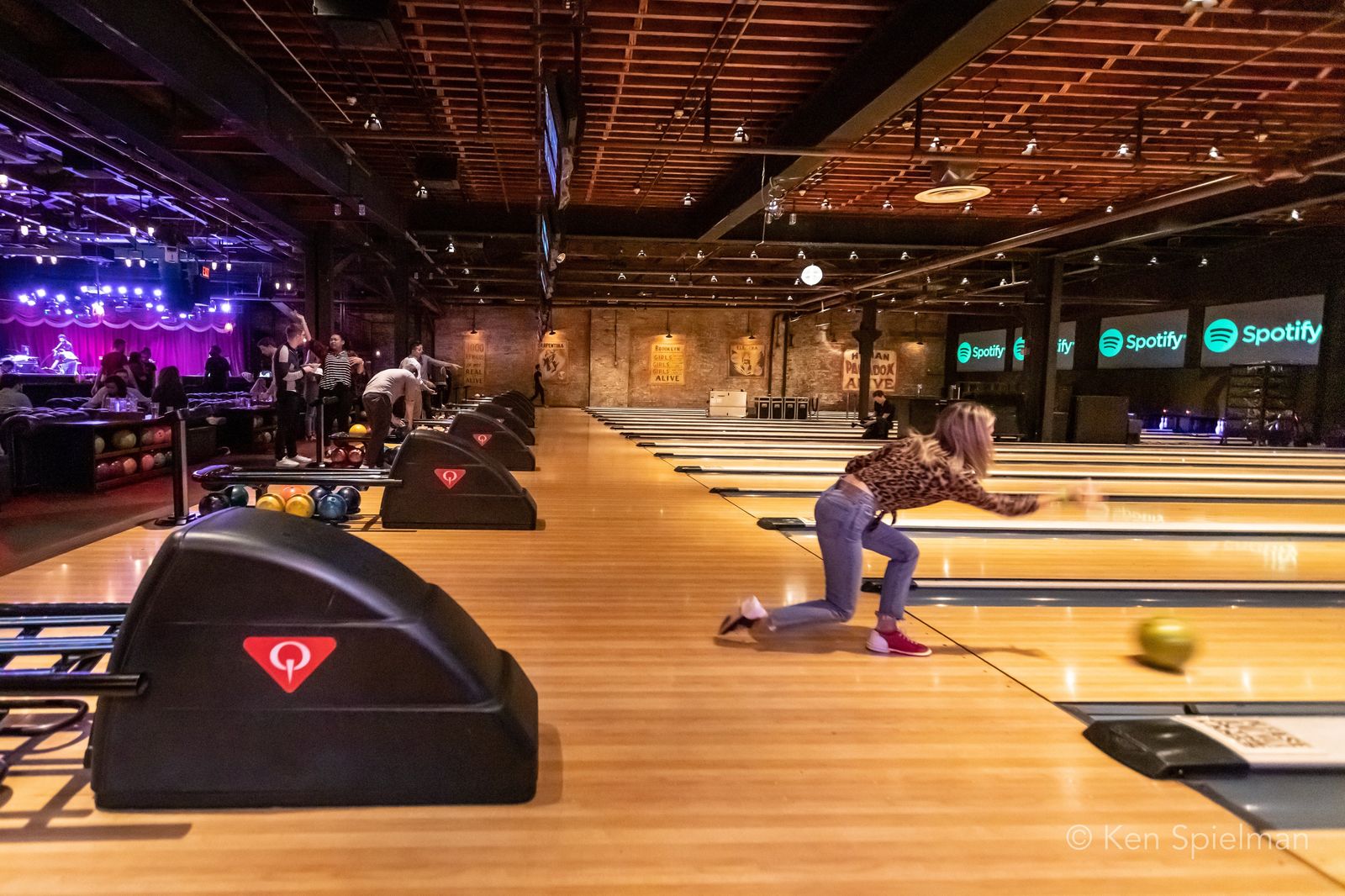 Rows of bowling lanes under a wood-beamed ceiling with one bowler crouching at a lane