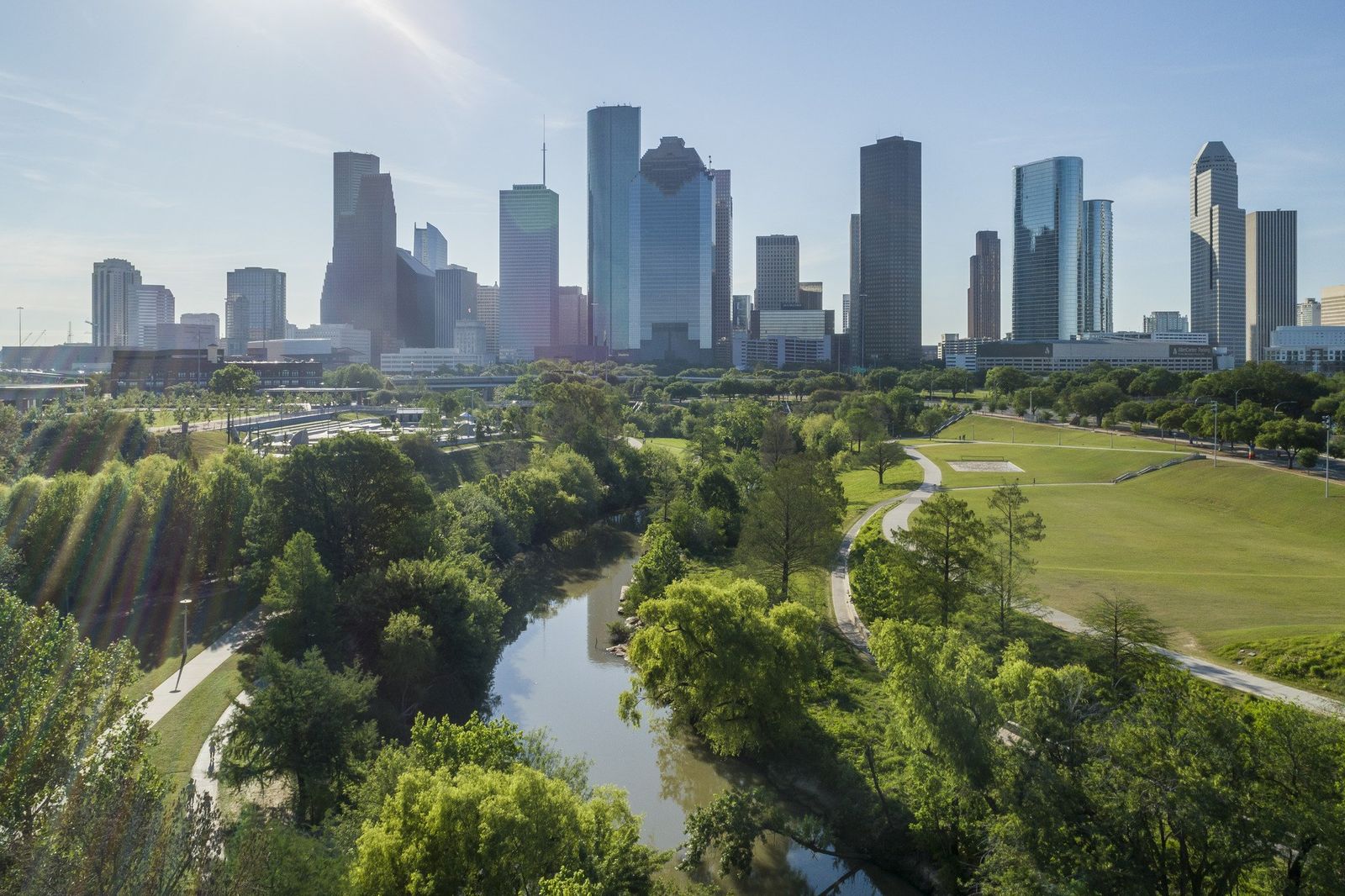 Aerial view of Buffalo Bayou winding through green parkland with the Houston skyline behind