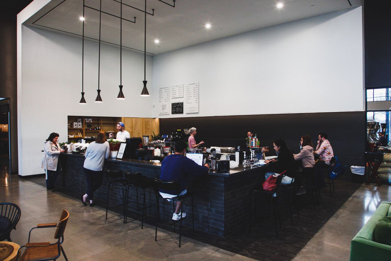 A cafe interior with a long dark counter, pendant lights and customers at tables.