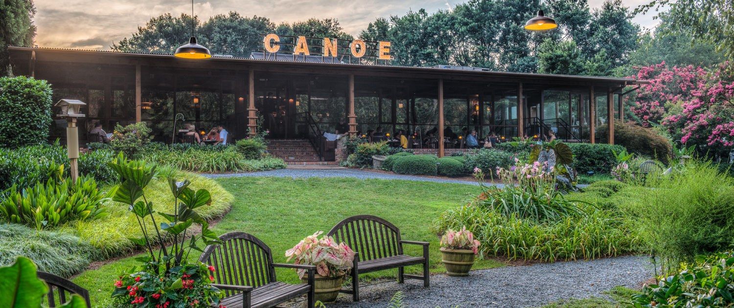 Restaurant building with a covered porch beside a landscaped garden lawn