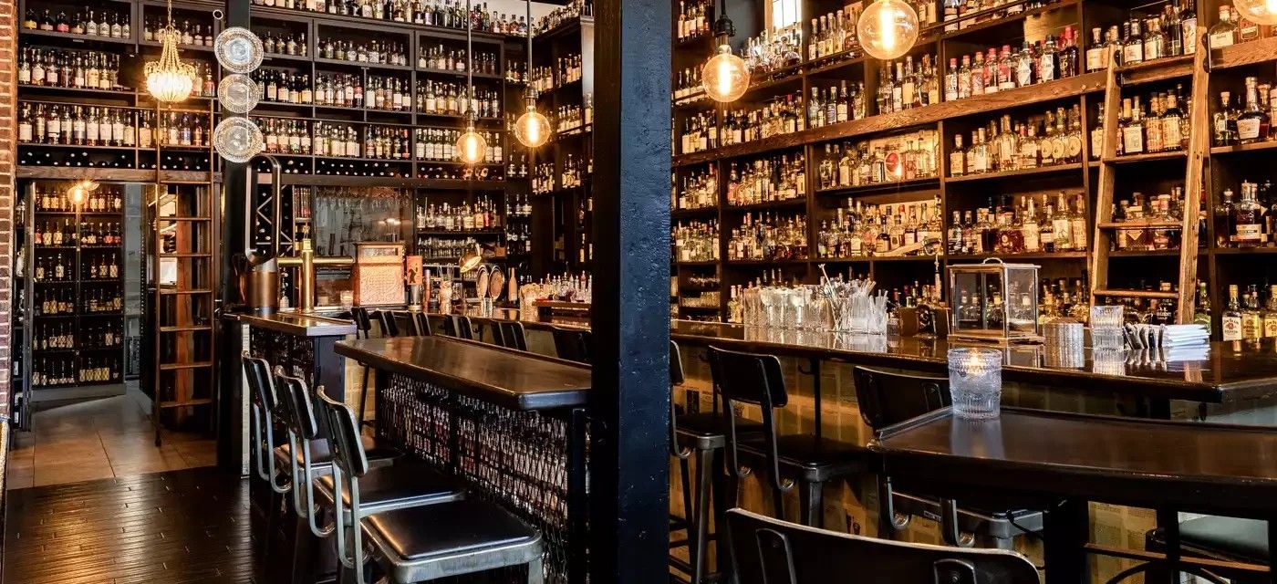 A long bar with stools in front of floor-to-ceiling shelves of bottles.