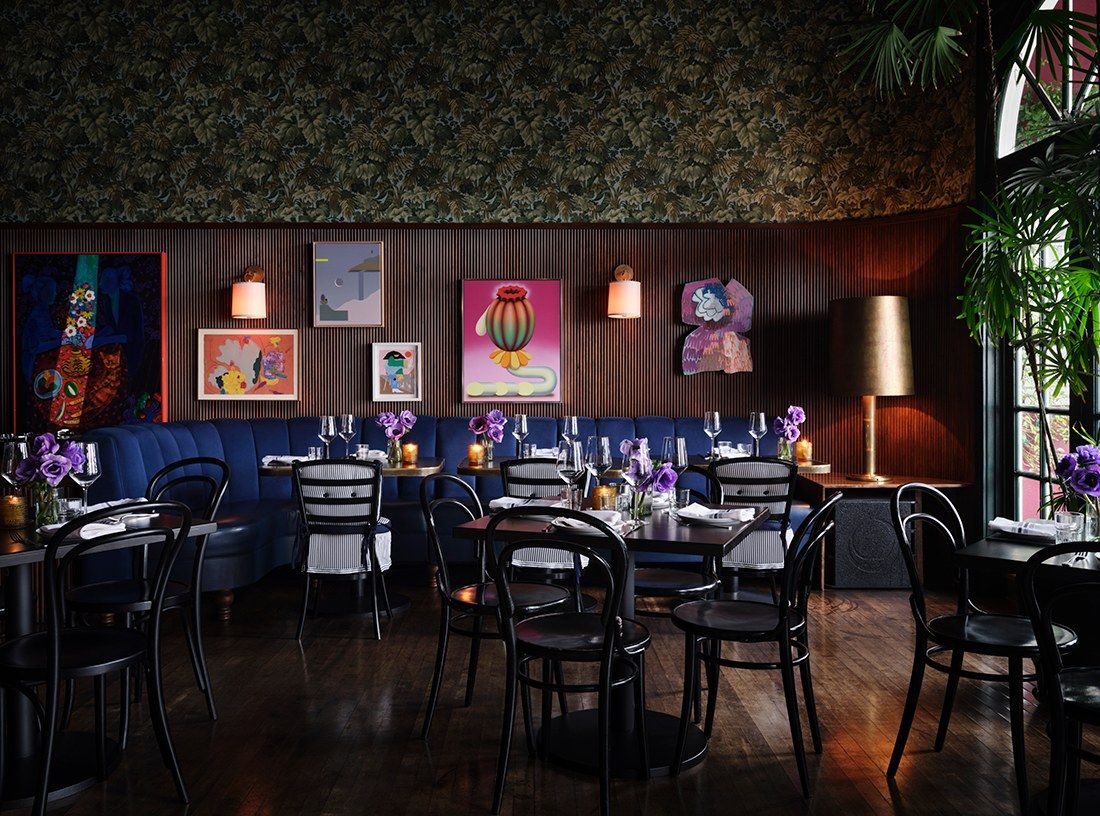 Dim dining room with dark wood walls, framed art and tables set with chairs
