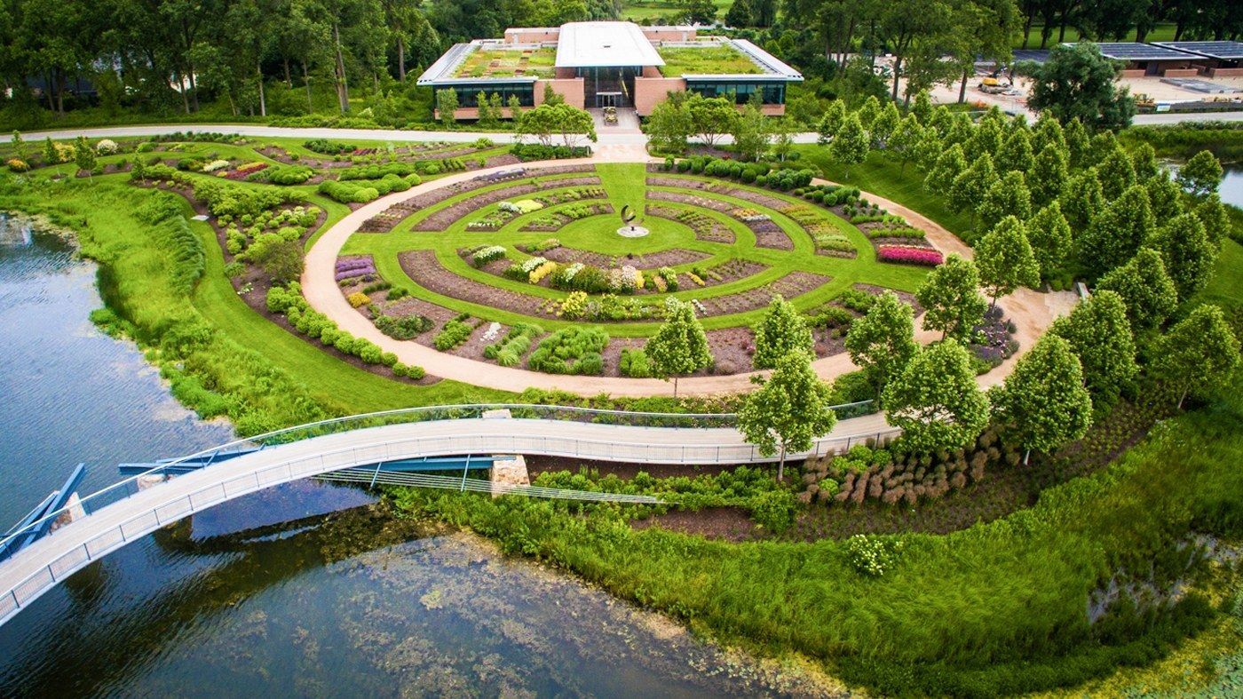 An aerial view of a circular hedge garden surrounded by water and a curving white footbridge.