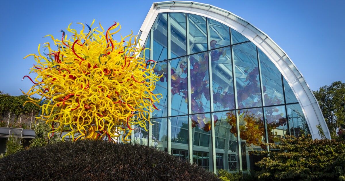 A yellow glass sculpture outside a curved glass building under a blue sky.