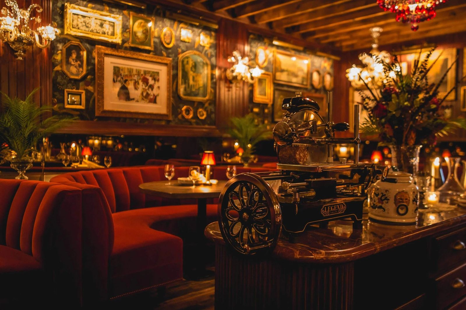 A warmly lit dining room with red leather booths, framed pictures on the walls and flowers on the tables.