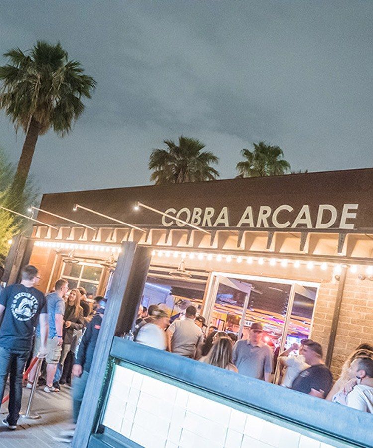 The Cobra Arcade sign over the lit entrance at dusk, with palm trees