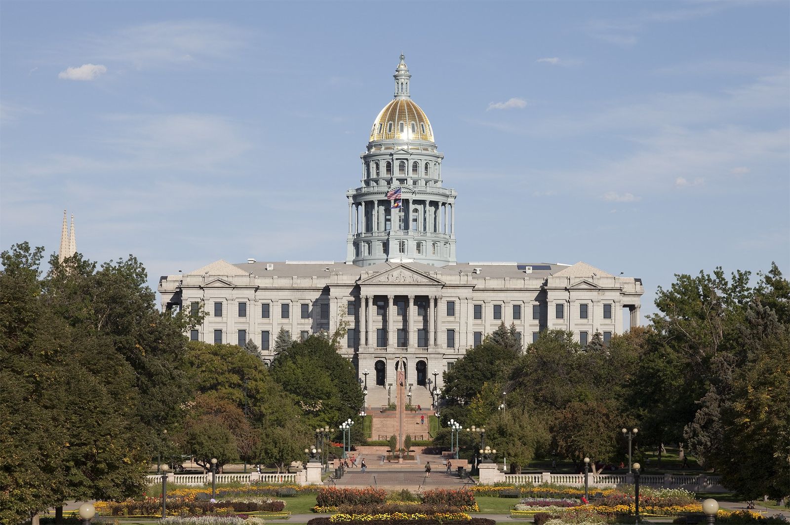 The domed capitol building behind a green lawn and trees under a clear sky.