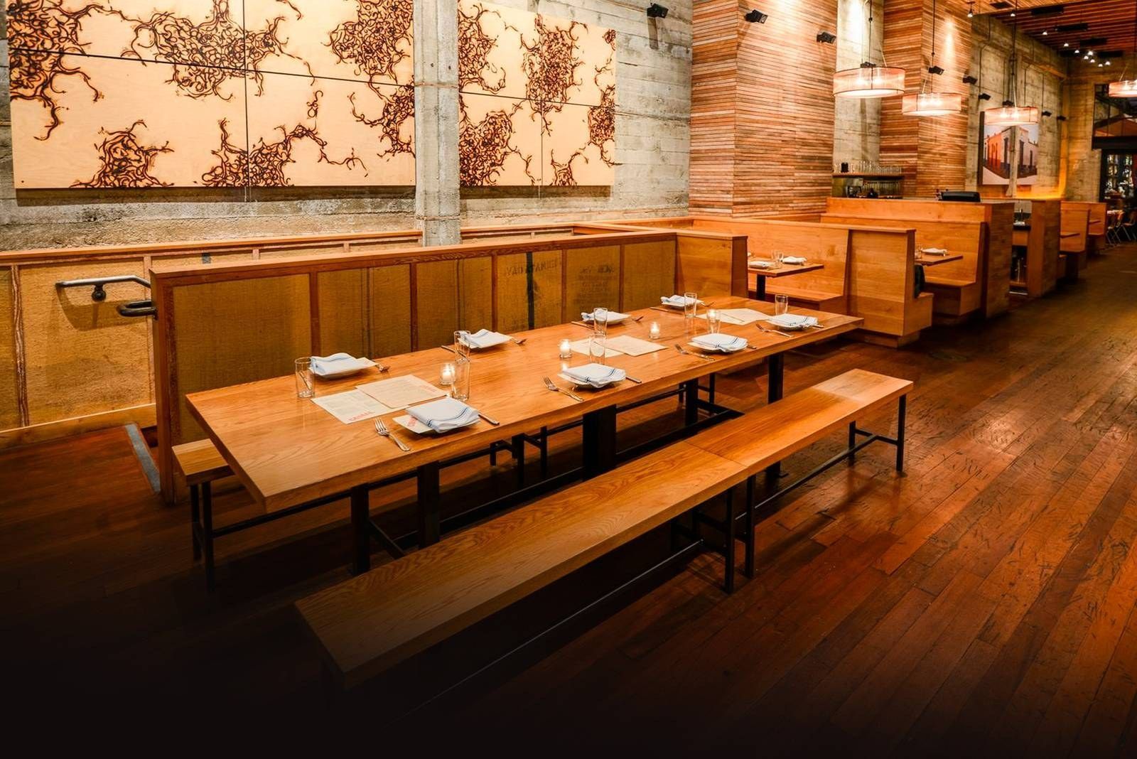 A long wooden dining room with communal tables, booths and wood-framed wall art.