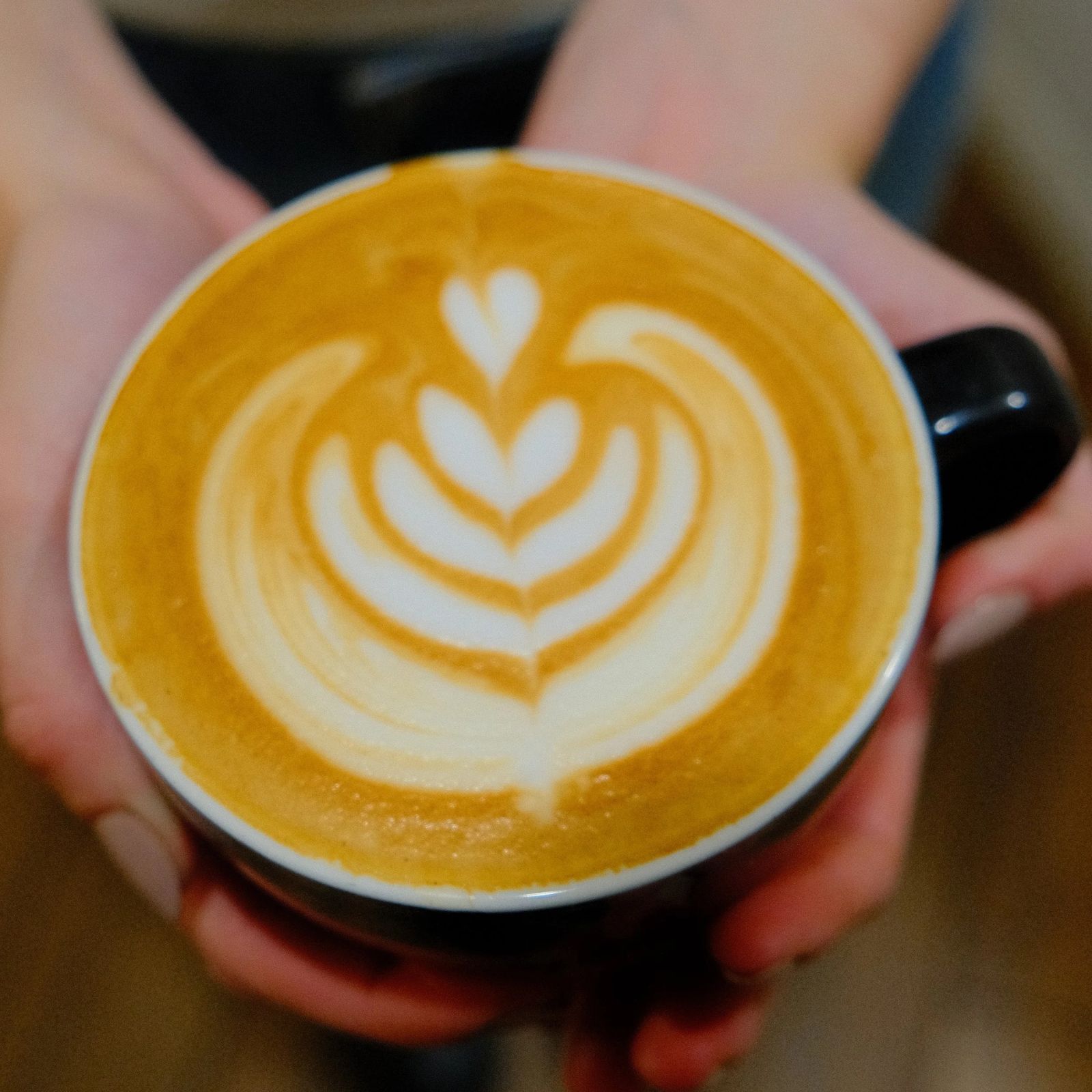 A hand holding a cup of latte with a heart-shaped latte art from above.