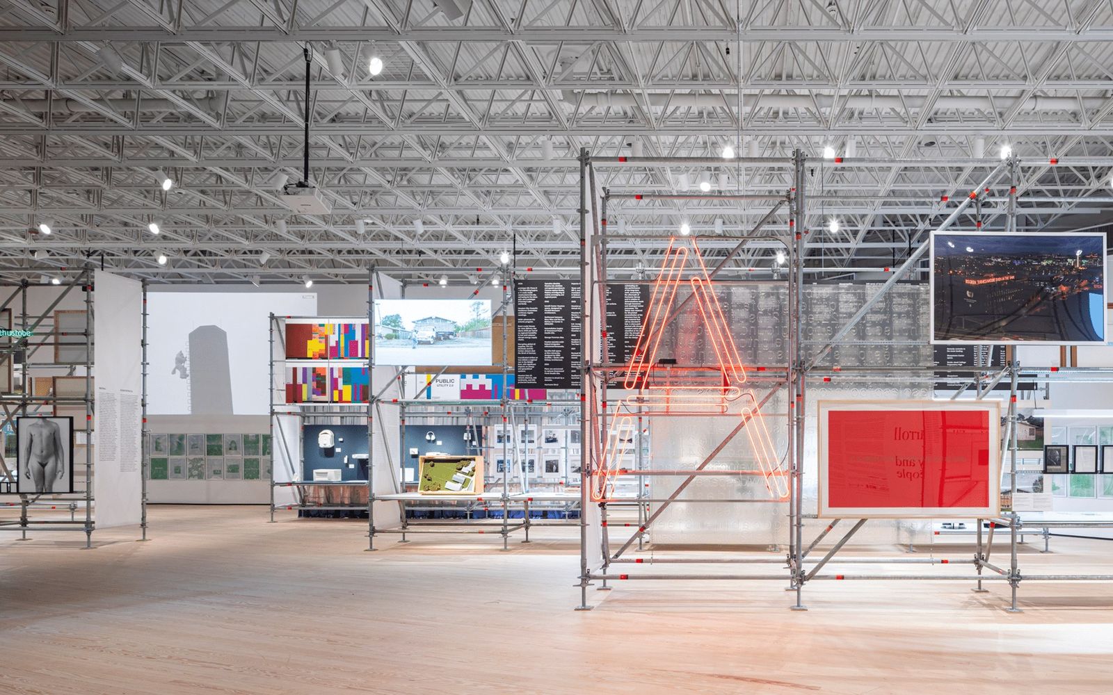 Empty gallery with a steel-truss ceiling and a large installation of shelves and red and silver pieces