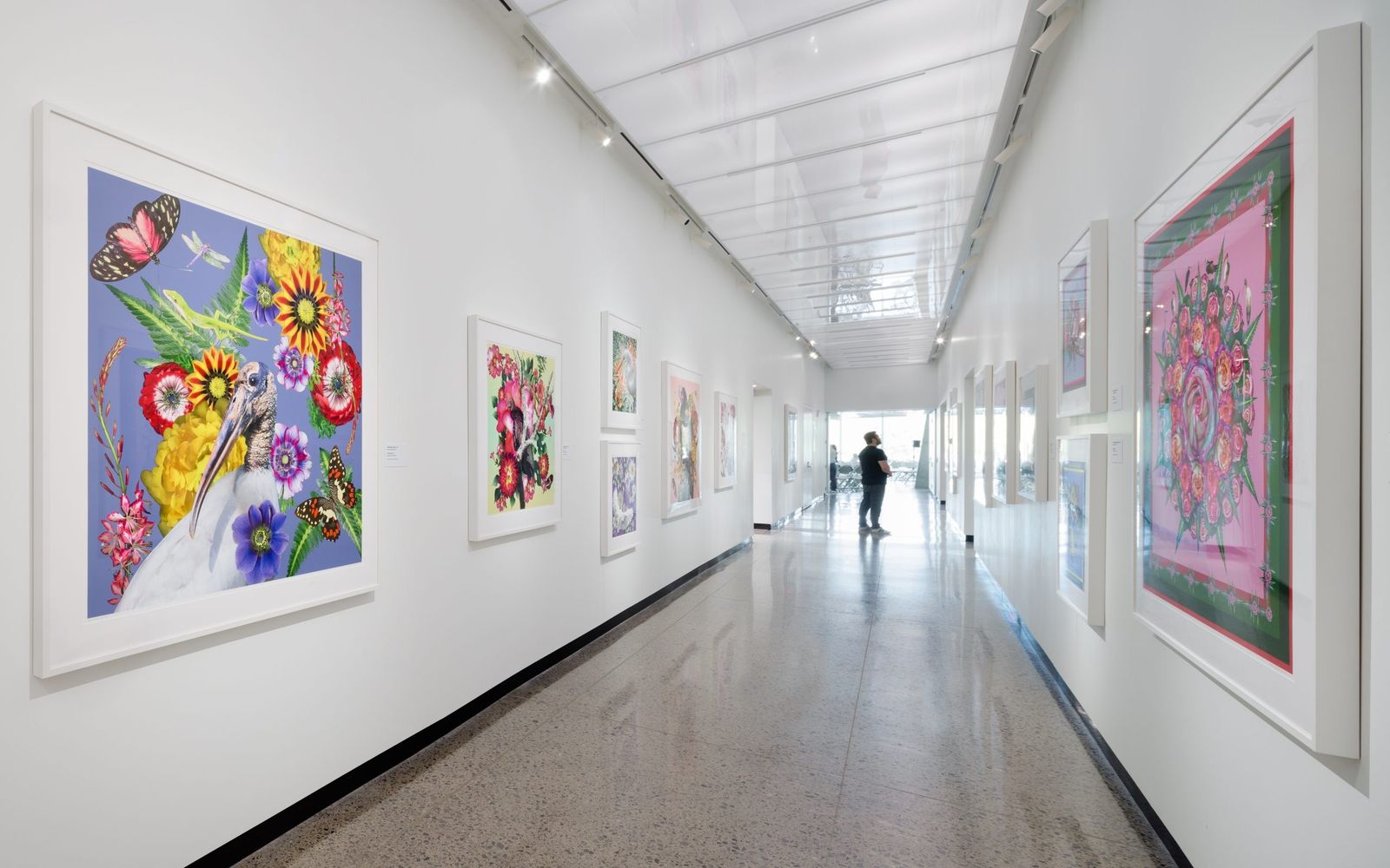A bright white gallery corridor with colorful framed textile art on the left wall.