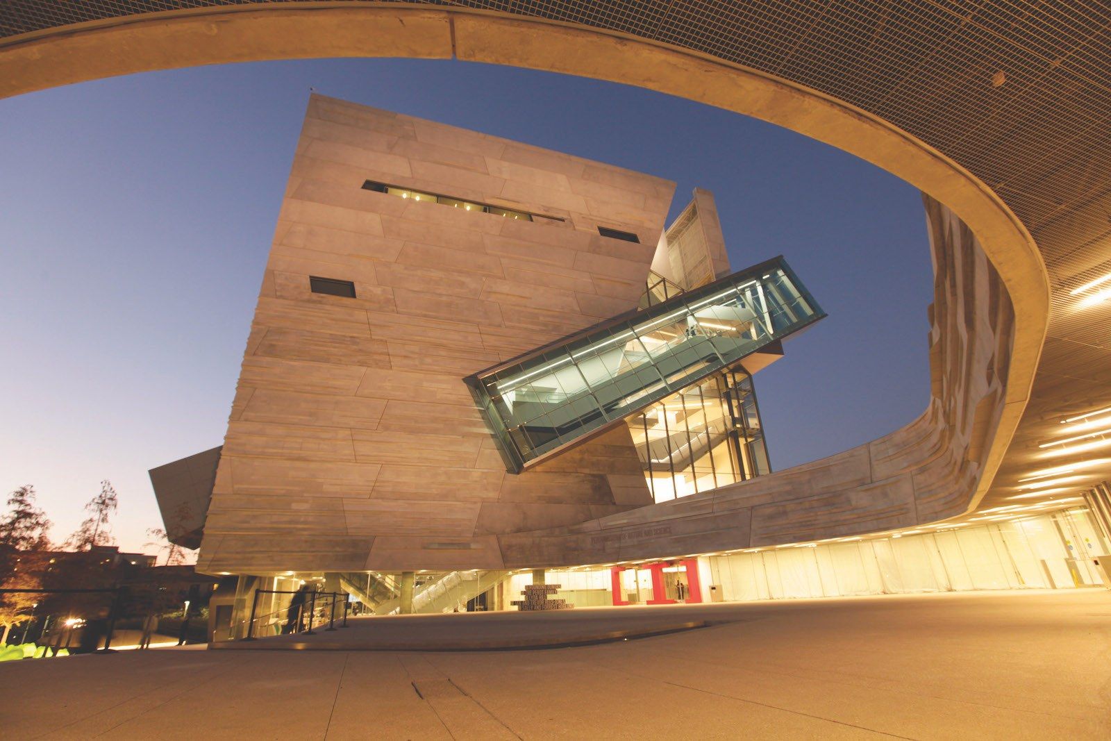 A sculptural museum building with a curved copper-toned roof lit at dusk.