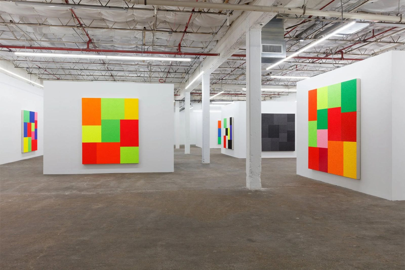 Large white gallery hall with colorful square-patterned paintings on the walls and white columns