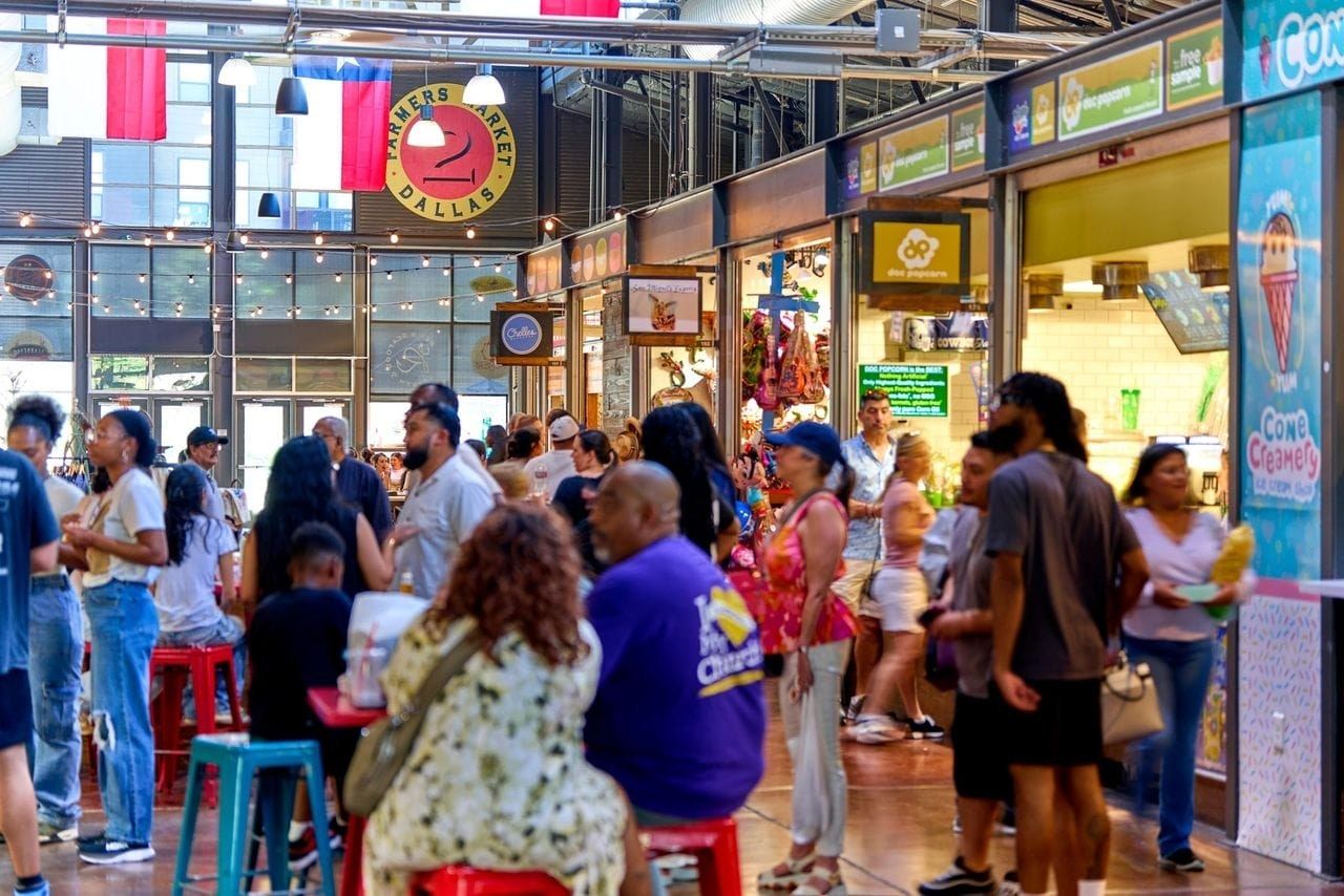 A crowded market hall with colorful food stalls, hanging signs and Texas flags.