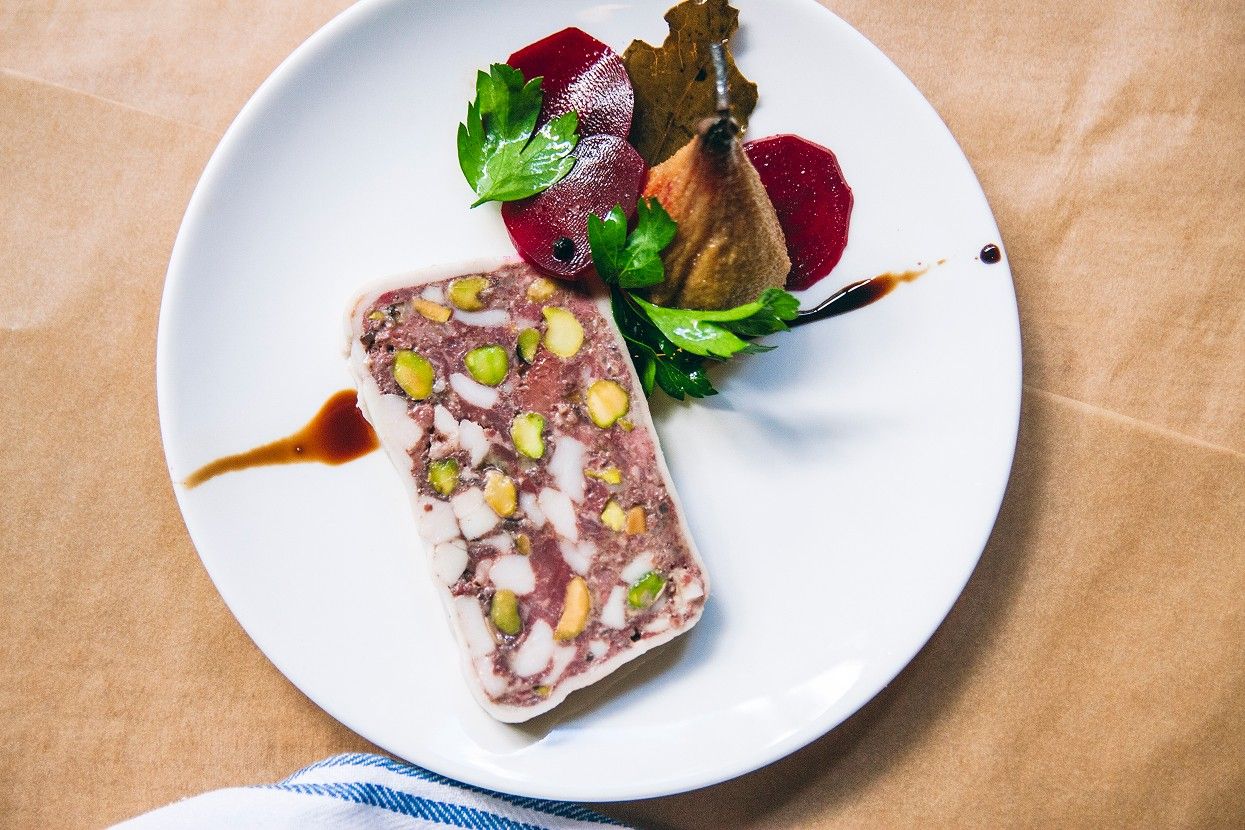 A slice of terrine with beets and herbs on a white plate set on brown paper.