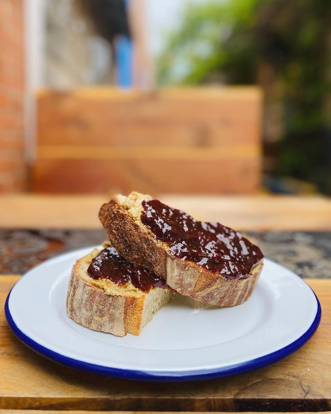 Two slices of toast with jam on a white plate with a blue rim, on a wooden table.
